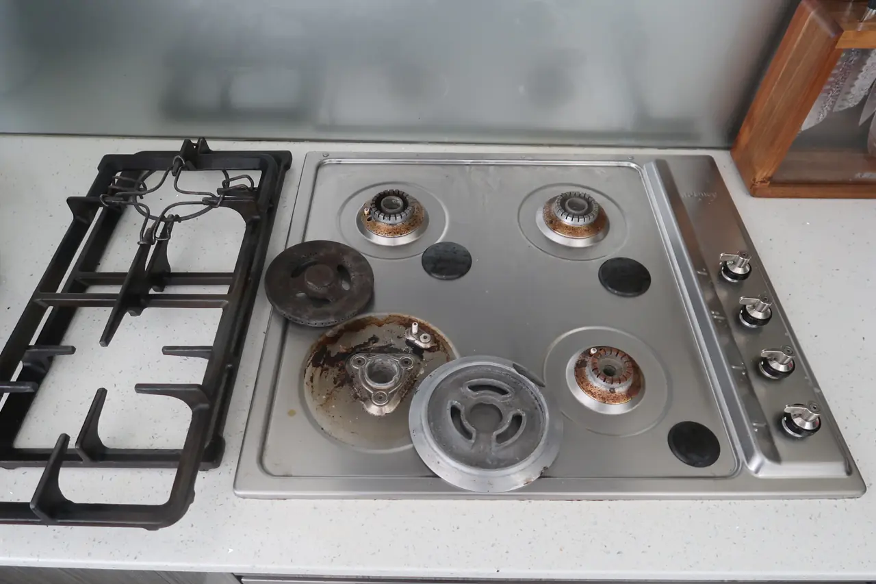 Gas stovetop with grates and burner caps removed, heavy grease and rust build-up